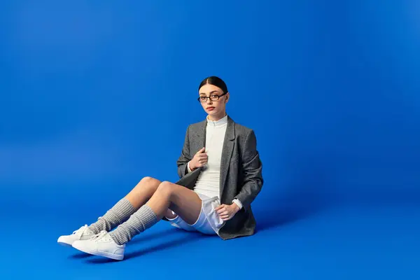 A beautiful young woman conveys a range of emotions while seated on a vibrant blue background. — Stock Photo