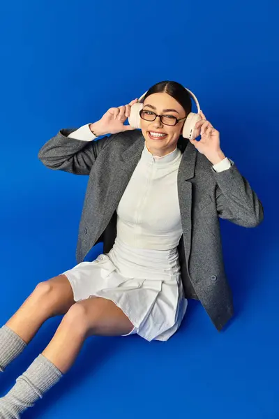 Happy woman listens to music with headphones, sitting on bright blue background in style. — Stock Photo