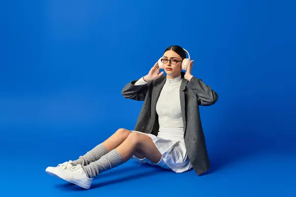 A young, beautiful woman sits on the floor, absorbed in music, with a vibrant blue wall behind her. — Stock Photo