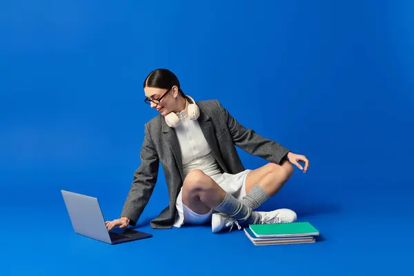 Young woman with her laptop, surrounded by colorful books in a vibrant blue space. — Stock Photo