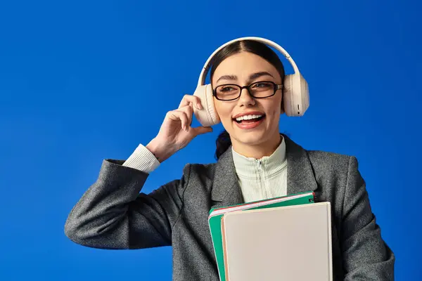 A beautiful young woman with glasses smiles joyfully, surrounded by colorful books and music. — Stock Photo