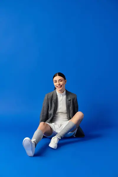 A young woman beams with happiness, sitting on a smooth blue surface in stylish comfort. — Stock Photo