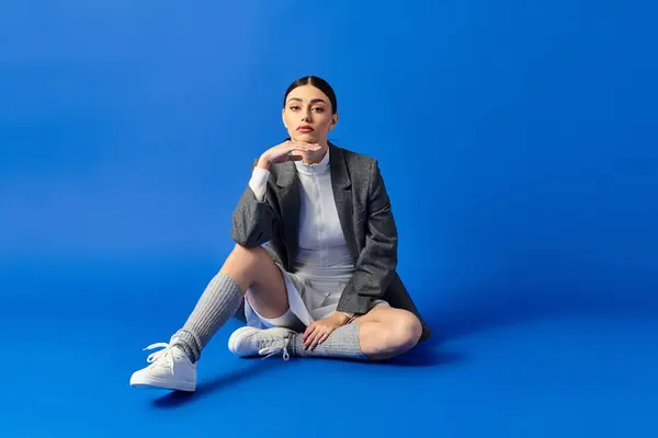 A young woman in a stylish outfit shows deep emotions against a vibrant blue backdrop. — Stock Photo