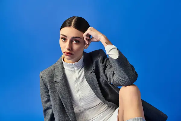 A young woman expresses deep emotions while seated gracefully, surrounded by bold blue color. — Stock Photo