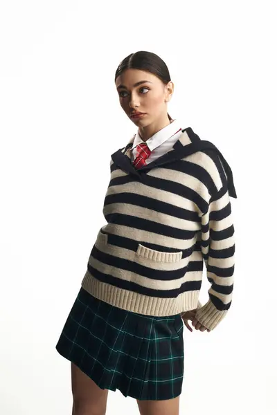 A young woman in a striped sweater and plaid skirt stands in a studio, sharing her emotions. — Stock Photo