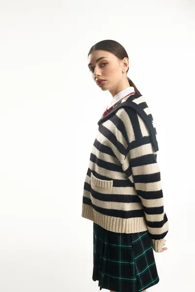 A young woman stands gracefully, showcasing her striped sweater in a soft, bright environment. — Stock Photo