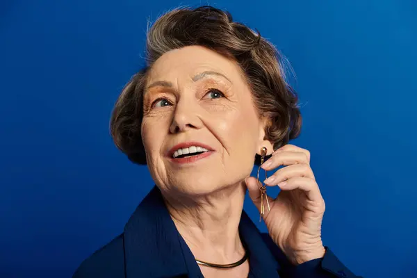Mujer madura exuda sofisticación en atuendo de moda, sonriendo calurosamente contra un entorno azul audaz. - foto de stock