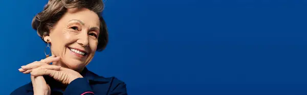 A graceful woman in her 60s models her stylish outfit against a striking blue backdrop, banner — Stock Photo