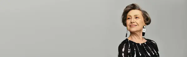 A beautiful woman in her 60s showcases elegance and style with confidence on a grey background, banner — Stock Photo