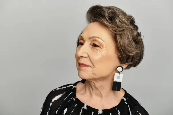A stylish woman in her 60s poses gracefully against a grey background, exuding confidence. — Stock Photo