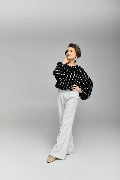 Una donna elegante nei suoi anni '60 modella con fiducia la moda elegante su uno sfondo grigio. — Foto stock