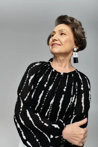 Una mujer impresionante en sus 60 años posa elegantemente sobre un fondo gris, exudando elegancia y estilo. - foto de stock