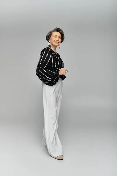 Una donna elegante nei suoi anni '60 posa con fiducia in abiti eleganti su uno sfondo grigio. — Foto stock