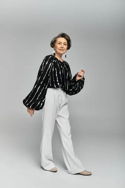Una donna sulla sessantina indossa un abbigliamento elegante, trasudando fiducia in uno sfondo grigio. — Foto stock