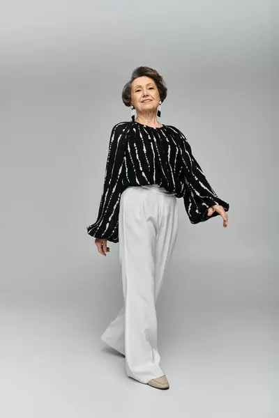 Una donna matura in abbigliamento elegante mette in mostra la bellezza senza tempo su uno sfondo grigio morbido. — Foto stock