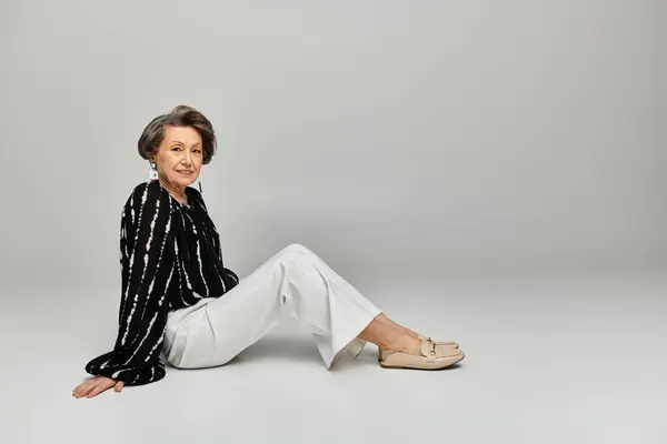 A beautiful woman in her 60s showcases elegant attire against a sleek grey background. — Stock Photo