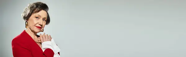 A stunning woman in her 60s poses confidently in stylish, elegant attire on a grey background, banner — Stock Photo