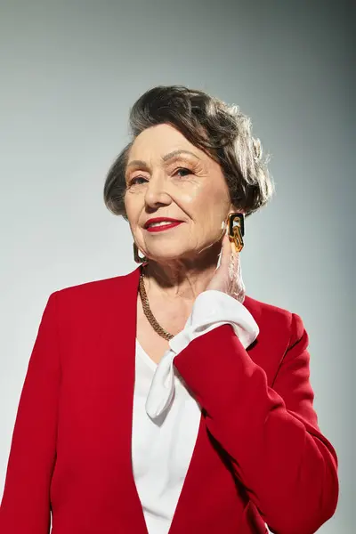A stylish woman in her 60s confidently poses against a grey background. — Stock Photo