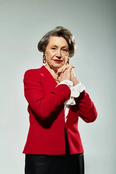 A sophisticated woman in her 60s poses gracefully against a grey background, radiating style. — Stock Photo