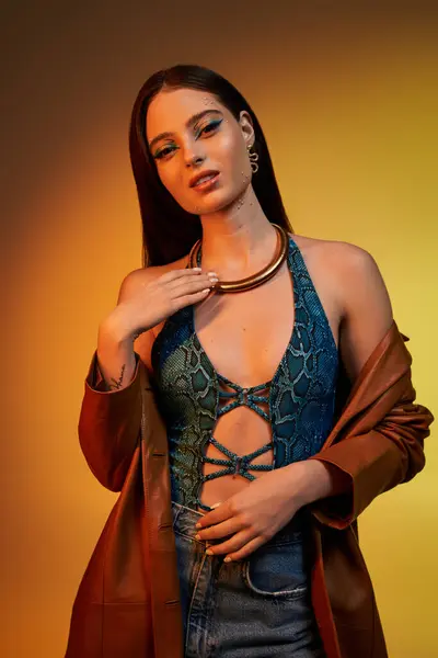 A young woman in snake print attire exudes confidence in a vibrant studio with striking lighting. — Stock Photo