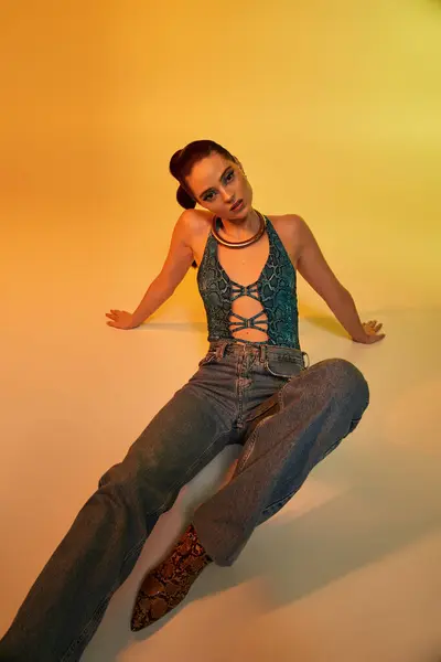 Young woman in fashionable snake print outfit poses confidently against a warm backdrop. — Stock Photo