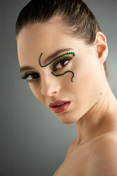 A beautiful young woman showcases striking snake makeup in a stylish studio environment. — Stock Photo