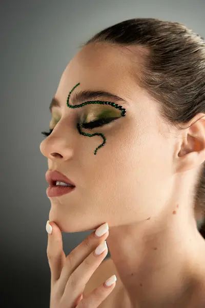 A beautiful young woman poses with mesmerizing snake makeup, radiating beauty in a studio setting. — Stock Photo