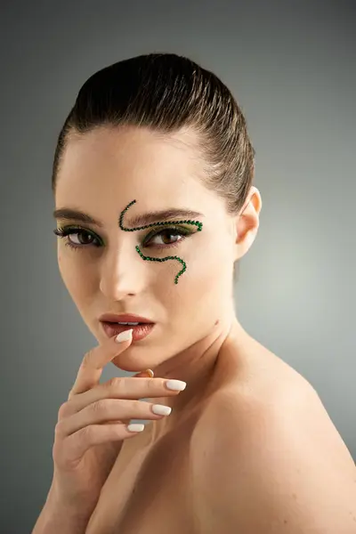 A beautiful young woman displays striking snake-themed makeup, posing elegantly in a studio. — Stock Photo