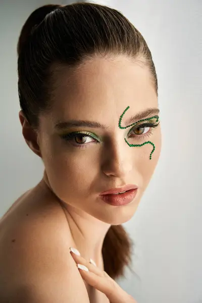 In a studio, a beautiful young woman displays striking snake makeup, emphasizing her features. — Stock Photo