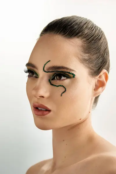 A young woman showcases stunning snake-inspired makeup while posing in a modern studio. — Stock Photo