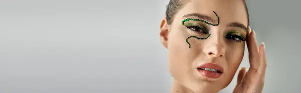 Beautiful young woman poses elegantly in a studio, displaying intricate snake makeup art, banner — Stock Photo