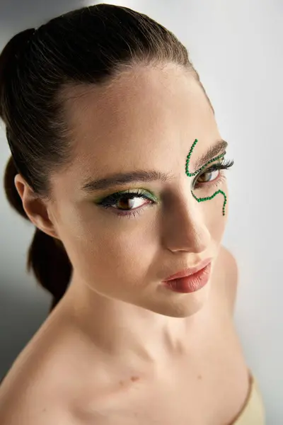 A beautiful young woman poses gracefully, showcasing intricate snake-inspired makeup in a studio. — Stock Photo