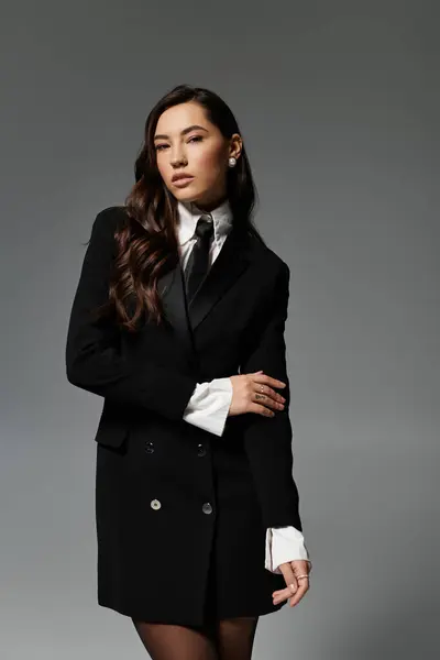 A young woman with long brown hair poses confidently in stylish clothes against a grey backdrop. — Stock Photo