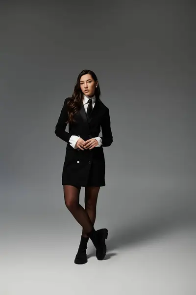 A beautiful young woman with long brown hair poses elegantly in stylish clothes against grey. — Stock Photo