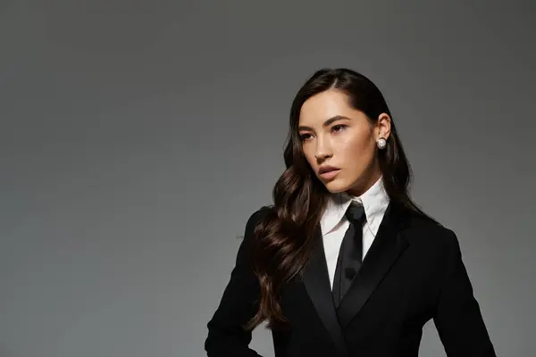 A young woman with long brown hair poses gracefully in stylish attire against a grey backdrop. — Stock Photo