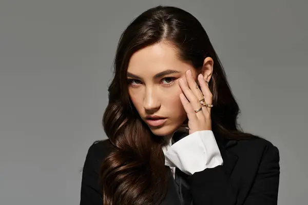 A stunning woman with long brown hair poses in a chic outfit against a grey backdrop. — Stock Photo
