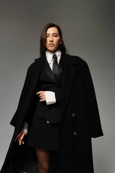 Elegant woman with long brown hair poses confidently in fashionable attire against a grey backdrop. — Stock Photo