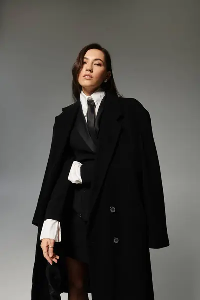A confident young woman with long brown hair poses in stylish clothes against a grey backdrop. — Stock Photo