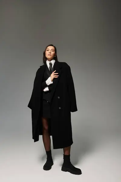 A young woman poses in a black outfit against a grey studio backdrop. — Stock Photo