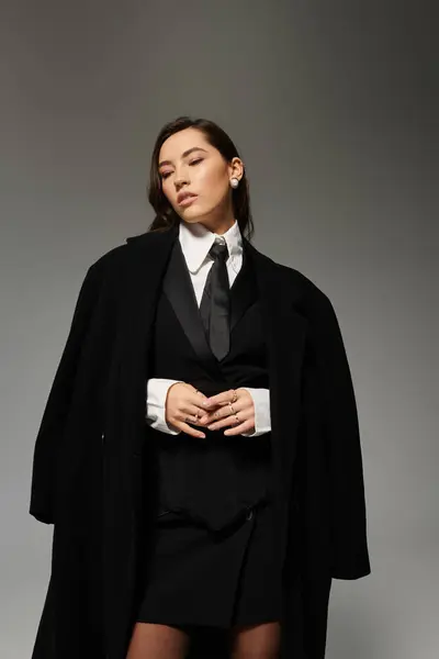 Una giovane donna sicura di sé posa con stile in uno studio grigio, mostrando il suo senso della moda. — Foto stock