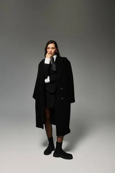 Eine selbstbewusste junge Frau posiert elegant im schicken Outfit vor grauem Hintergrund. — Stockfoto