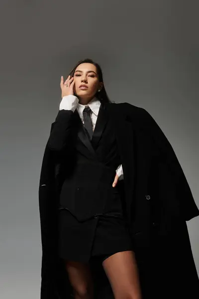 Una hermosa joven con el pelo castaño largo golpea una pose elegante en un traje elegante. - foto de stock