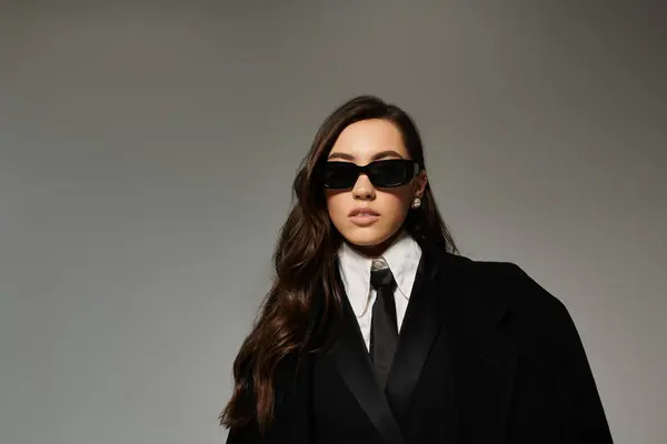 A beautiful young woman in a tailored suit showcases her fashion sense in a grey studio. — Stock Photo