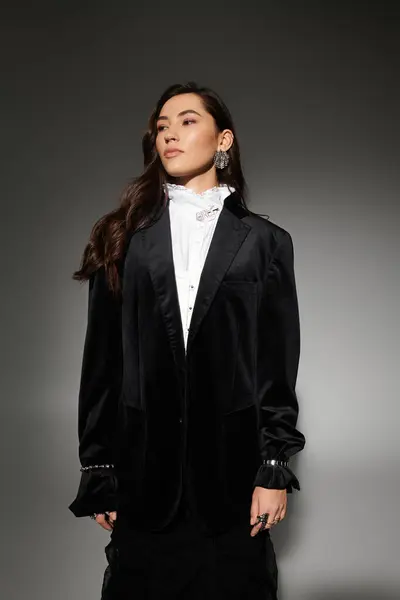 A young woman with shiny brown hair poses confidently in a chic outfit against a grey backdrop. — Stock Photo