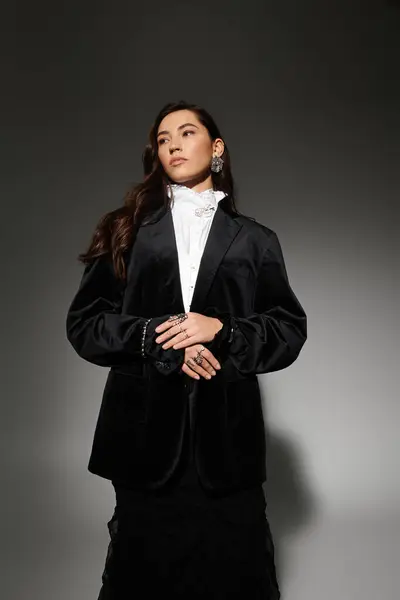 A young woman with shiny brown hair poses confidently in elegant attire against a grey backdrop. — Stock Photo