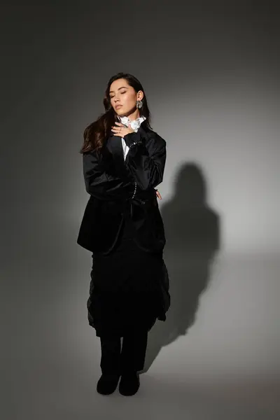 A young woman with shiny brown hair poses gracefully in an elegant outfit against a grey backdrop. — Stock Photo