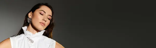 A young woman with shiny brown hair poses gracefully in a chic outfit against a grey backdrop, banner — Stock Photo