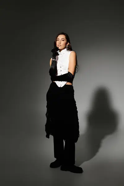 A young woman with shiny brown hair poses elegantly in chic attire against a grey backdrop. — Stock Photo