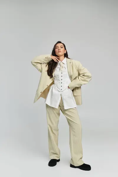 A beautiful woman dressed in a chic beige suit strikes a confident pose in a simple backdrop. — Stock Photo