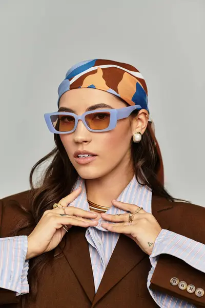 A young woman displays her trendy sunglasses and scarf against a neutral backdrop. — Stock Photo